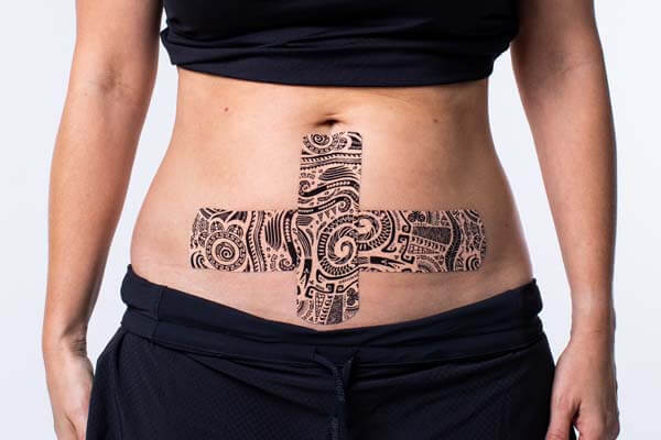 Final result showing tattoo print kinesiology tape in a cross shape on the lower abdomen.