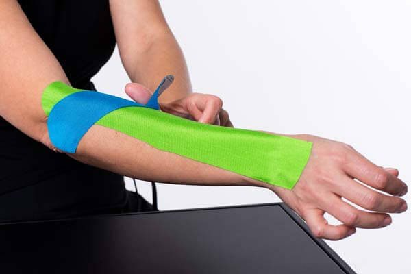 Blue kinesiology tape being applied in one smooth motion while the arm is rotated outward and extended.